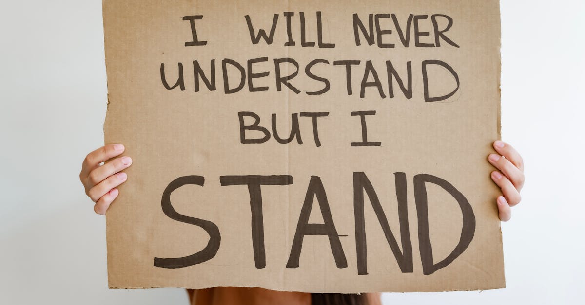 close up of hands holding a cardboard sign reading i will never understand but i stand